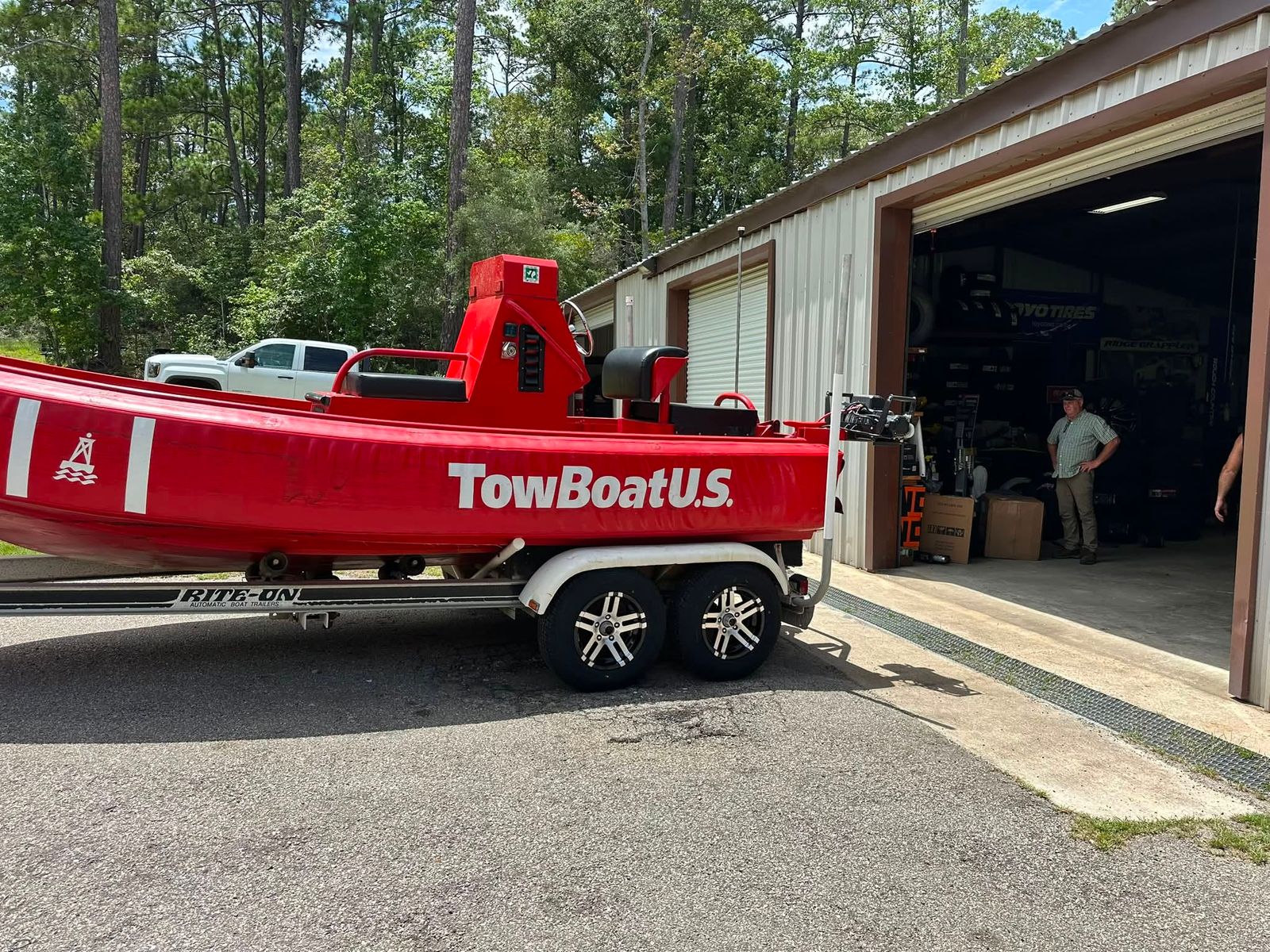 The red and white towing vessel at the service facility with staff visible in the open boat house.