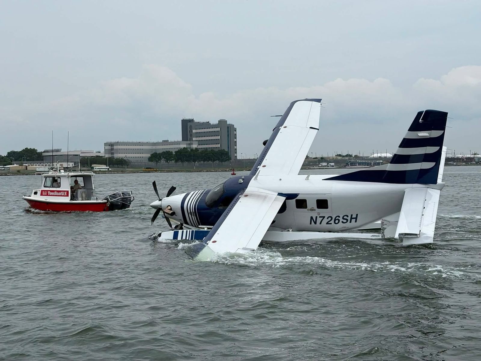 A seaplane partially submerged in the lake with a TowBoatUS vessel alongside it, responding to the scene.