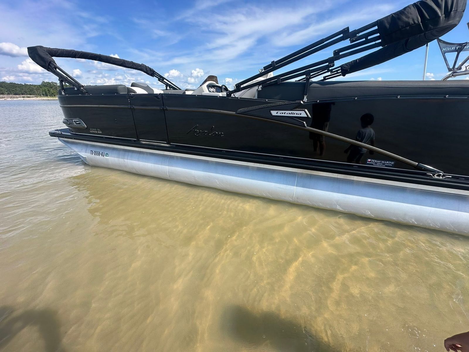 A black pontoon boat with its canopy extended, beached in shallow water on the reservoir.
