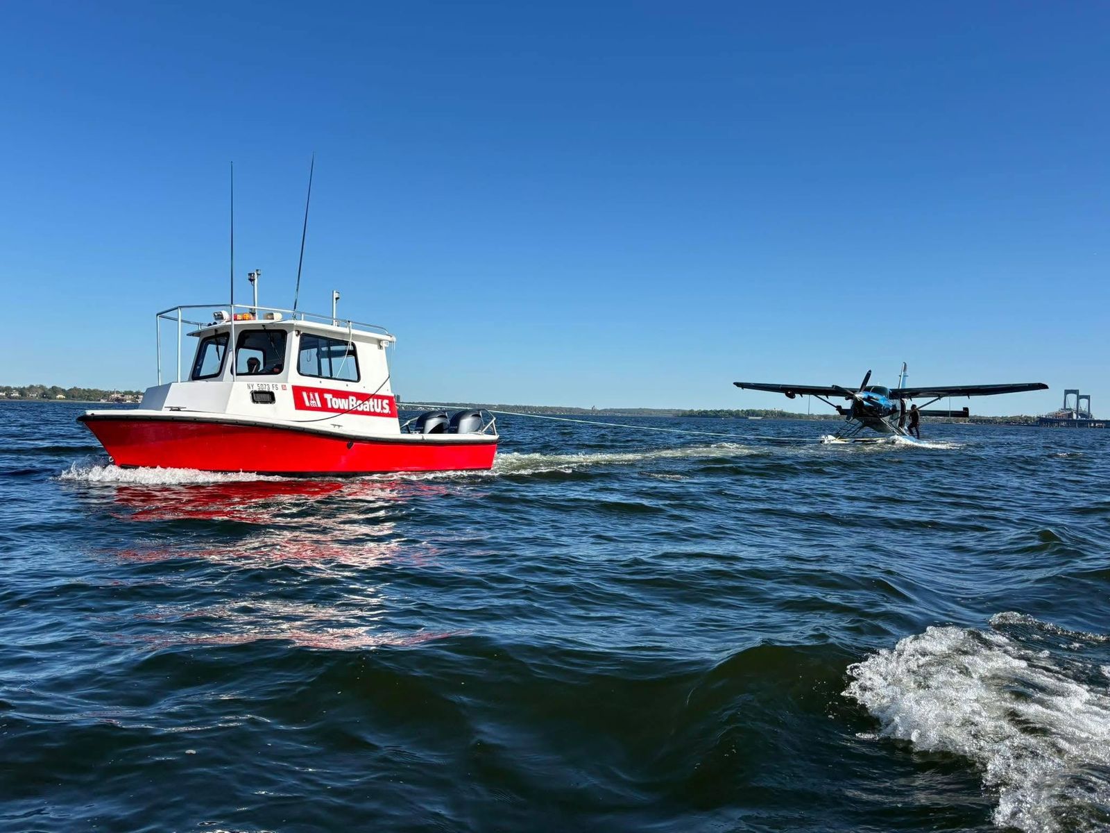 Red and white TowBoatUS service vessel on Sam Rayburn Reservoir with a seaplane in the background.