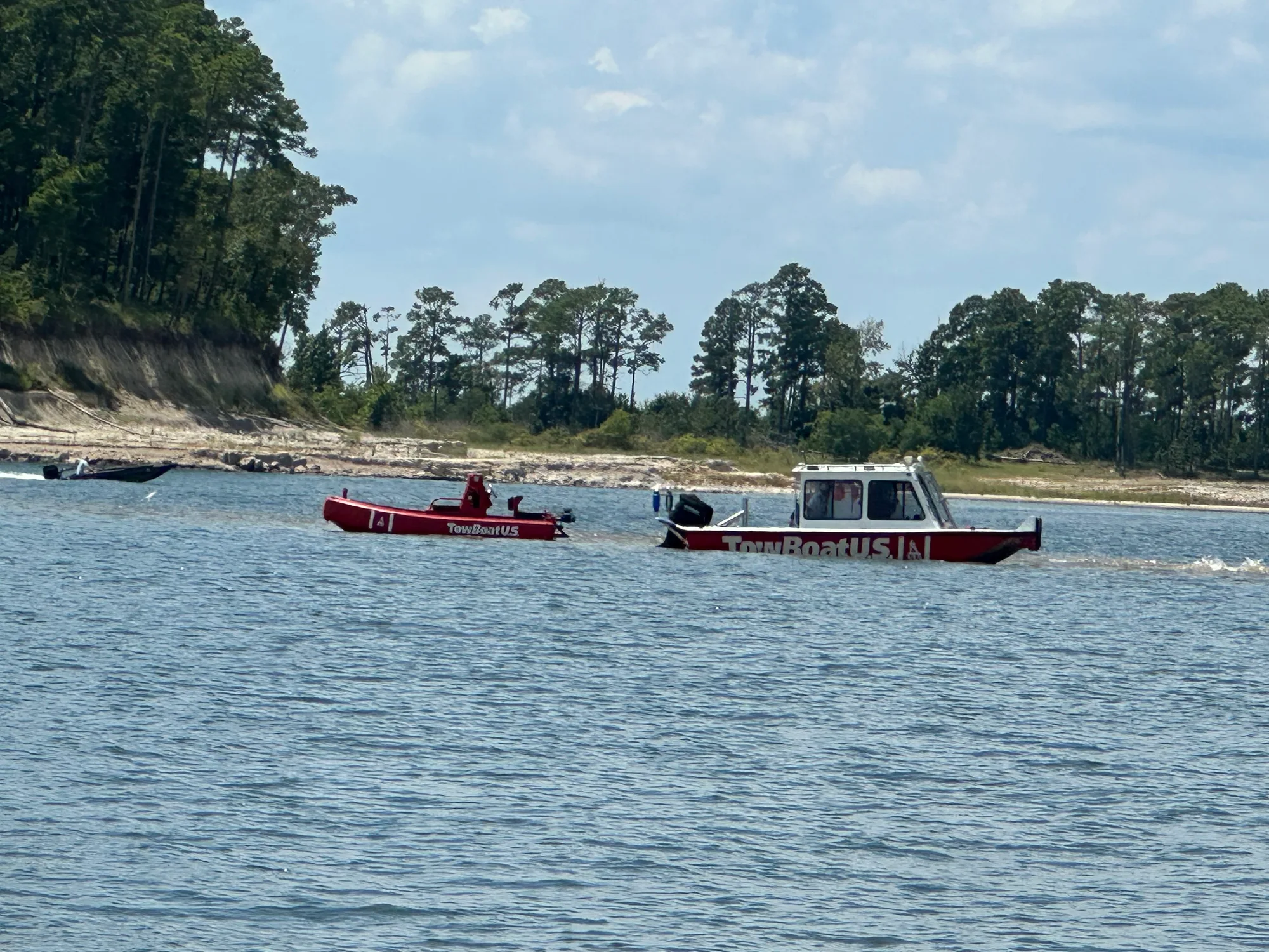 A TowBoatUS vessel towing a smaller boat across Sam Rayburn Reservoir, pine-covered shoreline behind them.
